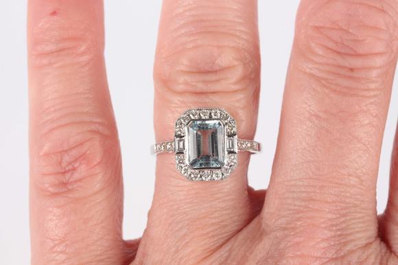 TooveysA white gold, aquamarine and diamond cluster ring, collet set with the cut cornered rectangular step cut aquamarine within a surround of baguette and