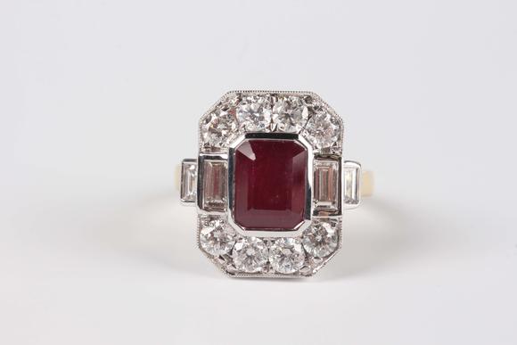 TooveysAn 18ct two colour gold, ruby and diamond cluster ring, collet set with the cut cornered rectangular step cut ruby within a surround of baguette and c