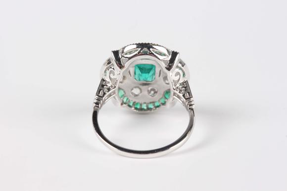 TooveysA platinum, emerald and diamond ring in an Art Deco inspired cluster design, mounted with the cut cornered rectangular step cut emerald within a quatr