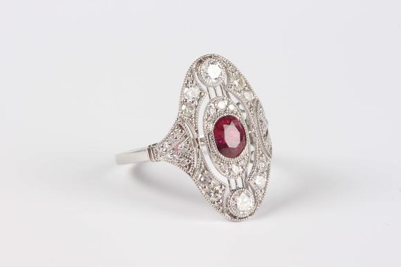 TooveysA platinum, ruby and diamond oval ring in an Art Deco inspired design, collet set with the oval cut ruby at the centre, detailed ‘Pt950’, weight 4.5
