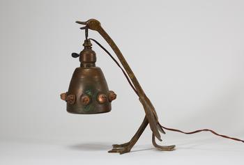 Lampe de table Art déco en métal patiné figurant un échassier stylisé soutenant une bobèche suspendue, ornée de cabochons en relief. Travail des année