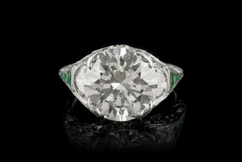Bague Art Déco platine centrant un diamant taille brillant entouré de diamants taille demi-lune et 8/8 ainsi que d'émeraudes calibrées<br><br><i>Art Déco platinum ring set with one center diamond, half-moon and 8/8 cut diamonds and calibrated-cut emeralds</i>